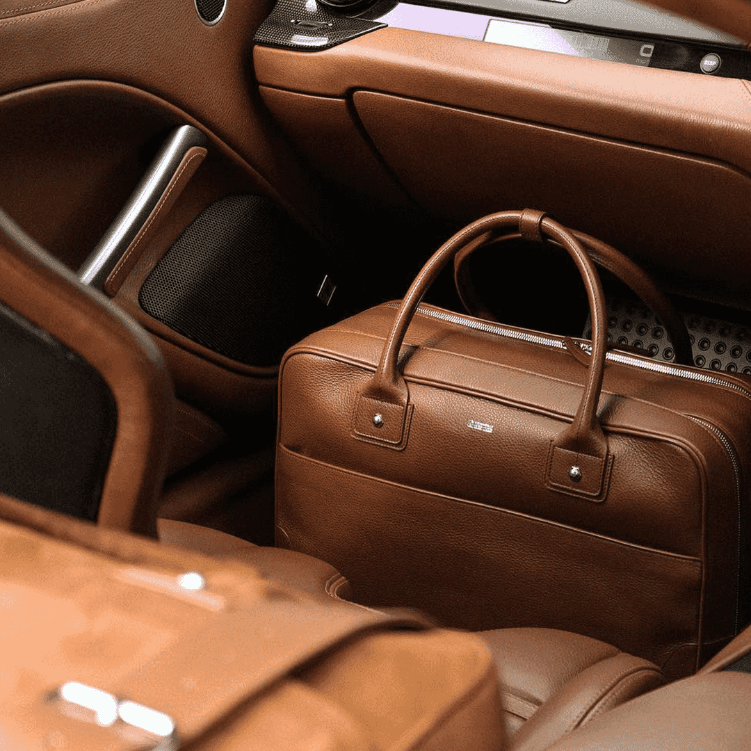 A brown leather briefcase inside a high-end car with tan leather interior.