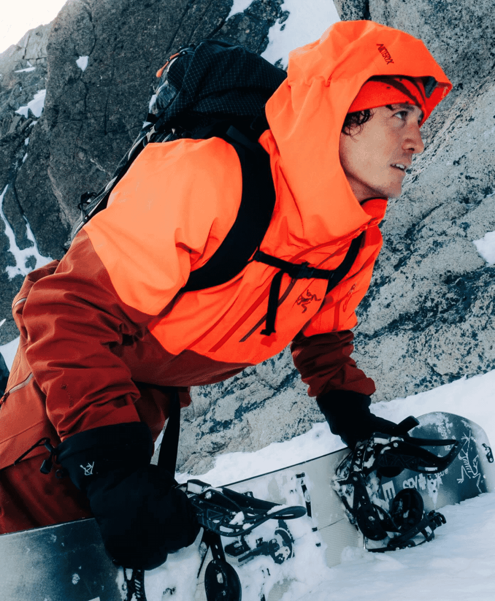 Snowboarder in a bright orange Arc'teryx technical jacket and pants.