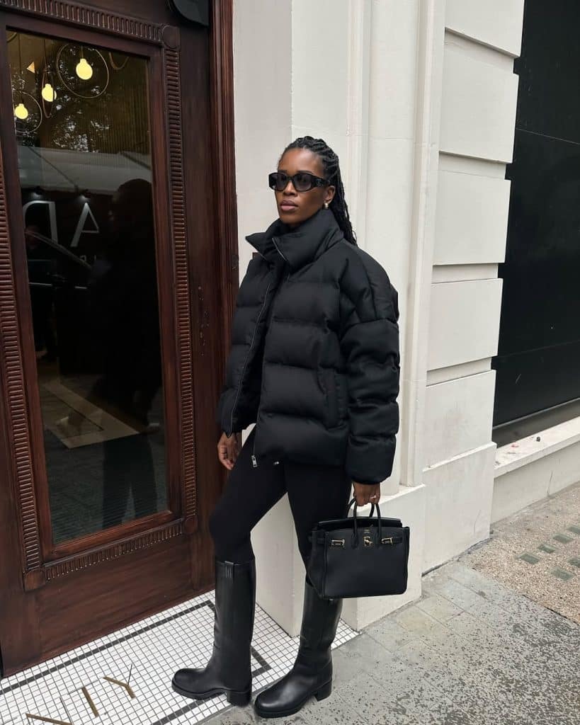Woman in an all-black puffer jacket and leggings tucked into knee-high boots.