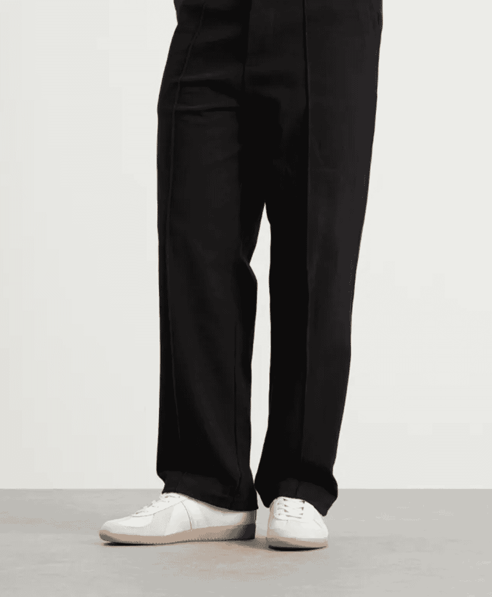 A person in wide-leg black trousers paired with white low-top sneakers.