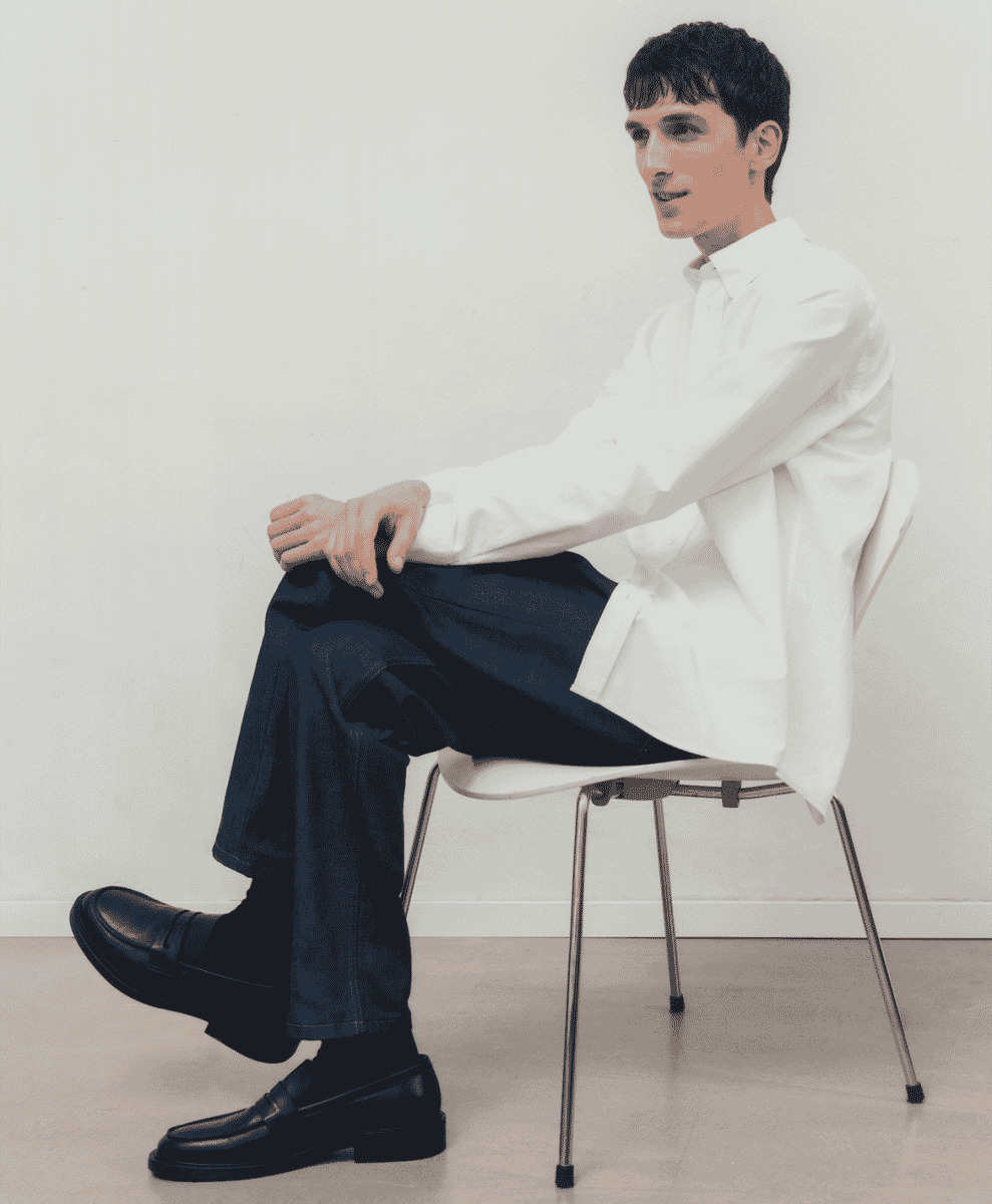 A man sitting wearing dark wide-leg trousers and black leather loafers.