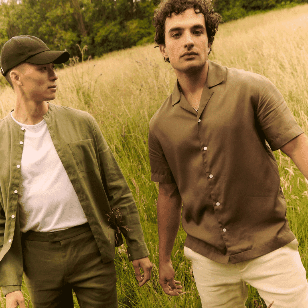 Two men in coordinated earth-toned outfits walking through a grassy field.