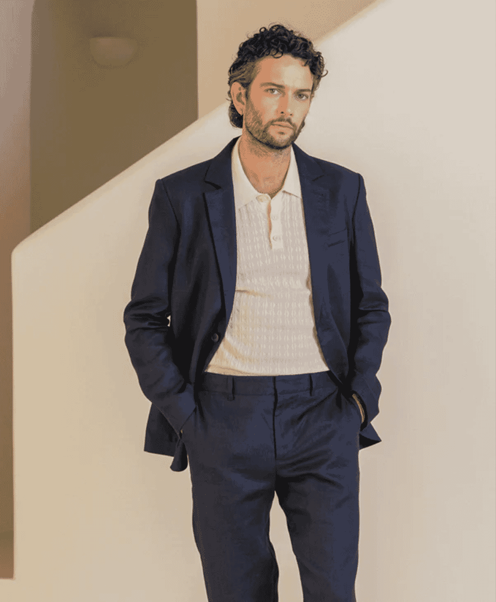 A man in a midnight navy blazer over a textured white polo shirt in a minimalist architectural setting.