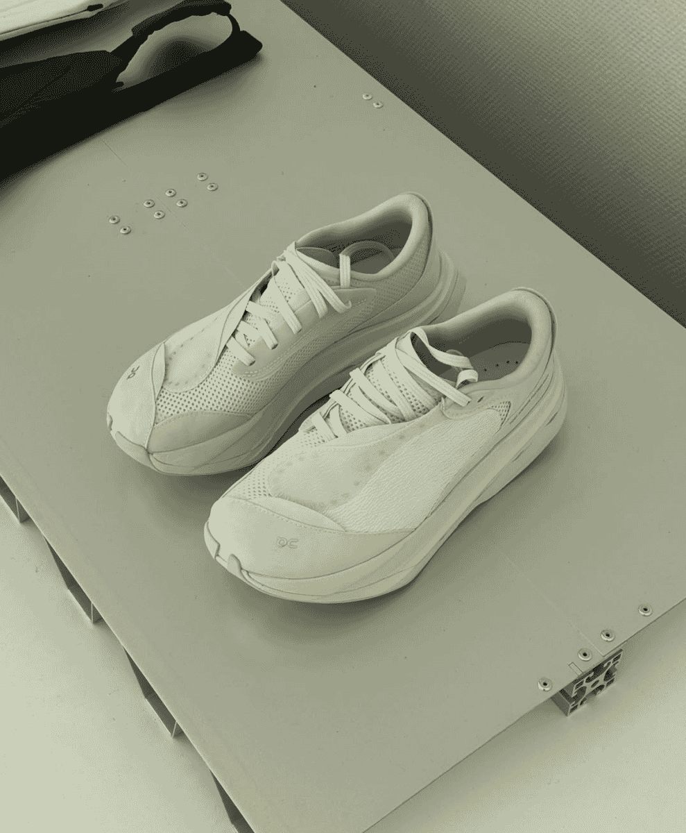 Close-up of a white On running sneaker with technical mesh on an industrial metal surface.