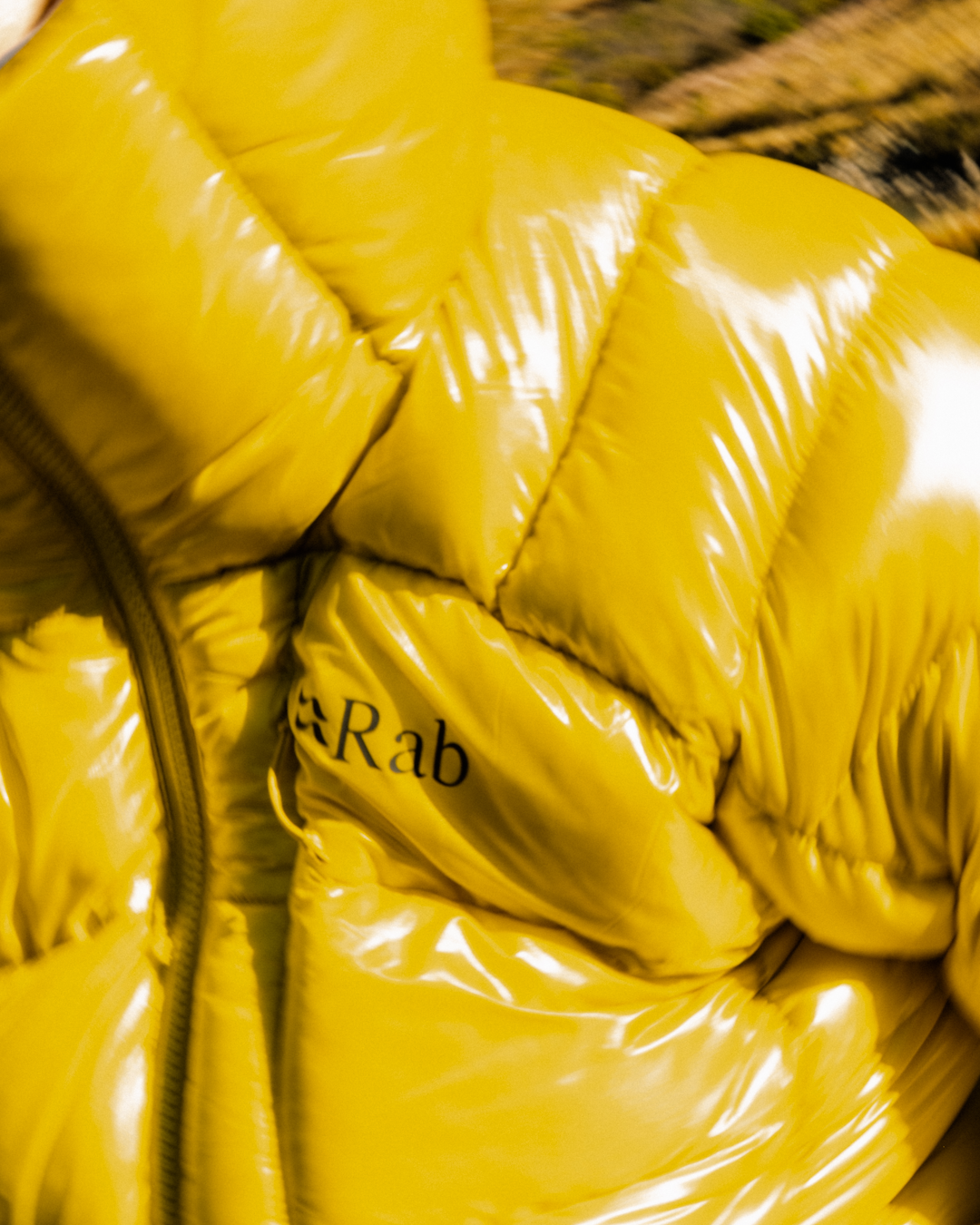 Close-up of a glossy yellow Rab puffer jacket showing quilted stitching and logo detail.